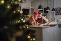 Cute little girl in red Santa hat with mother making homemade Christmas gingerbread cookies using cookie cutters together in home Royalty Free Stock Photo