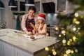 Cute little girl in red Santa hat with mother making homemade Christmas gingerbread cookies using rolling pin together in home Royalty Free Stock Photo