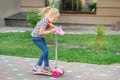 Cute little girl riding scooter in city park on bright summer day. Blond toddler having fun on street. Active leisure Royalty Free Stock Photo