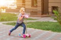 Cute little girl riding scooter in city park on bright summer day. Blond toddler having fun on street. Active leisure Royalty Free Stock Photo