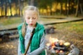 Cute little girl roasting marshmallows on stick at bonfire. Child having fun at camp fire. Camping with children in fall forest. Royalty Free Stock Photo