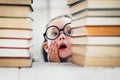 Cute little girl in round shaped glasses scared by too many books that she have to read. Study and education concept