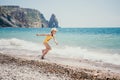 Cute little girl running along the seashore against a clear blue sea and rejoices in the rays of the summer sun Royalty Free Stock Photo