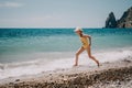 Cute little girl running along the seashore against a clear blue sea and rejoices in the rays of the summer sun Royalty Free Stock Photo