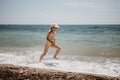 Cute little girl running along the seashore against a clear blue sea and rejoices in the rays of the summer sun Royalty Free Stock Photo