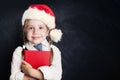 Cute little girl in Santa hat with book. Happy Child on empty blackboard background with copy space Royalty Free Stock Photo