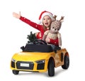 Cute little girl in Santa hat with Christmas tree and deer toy driving children`s car on white background Royalty Free Stock Photo