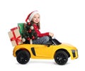 Cute little girl in Santa hat with Christmas tree and gift boxes driving children`s electric toy car on white background Royalty Free Stock Photo