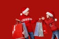 Cute little girl in Santa hat hanging shopping bag with Christmas gifts on hand of astonished boy during holiday Royalty Free Stock Photo