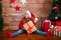 Cute little girl in Santa hat with present gift boxes sitting near tree at home Royalty Free Stock Photo