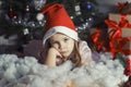 Cute little girl in santa hat is sad by the christmas tree