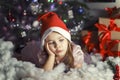 Cute little girl in santa hat is sad by the christmas tree