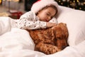 Cute little girl in Santa hat sleeping in bed near her English Cocker Spaniel. Christmas celebration