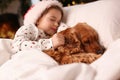 Cute little girl in Santa hat sleeping in bed near her English Cocker Spaniel. Christmas celebration