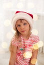 Cute little girl in Santa's hat enjoying at home. Holiday lights