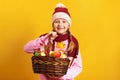 Cute little girl in a scarf and hat on a yellow background. A child holds a basket of apples. Royalty Free Stock Photo