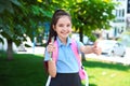 Cute little girl in school uniform with  and stationery showing thumbs-up on street Royalty Free Stock Photo