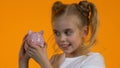 Cute little girl shacking piggy bank with coins and smiling, personal savings