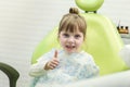 Cute little girl showing thumb up sign at dentist`s office clin