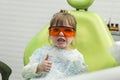 Cute little girl showing thumb up sign at dentist`s office clin