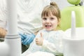 Cute little girl showing thumb up sign at dentist`s office clin