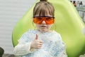 Cute little girl showing thumb up sign at dentist`s office clin