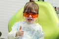 Cute little girl showing thumb up sign at dentist`s office clin