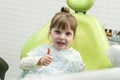 Cute little girl showing thumb up sign at dentist`s office clin