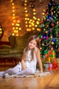 Cute little girl sits on the floor in the evening in the room near the festive Christmas tree Royalty Free Stock Photo