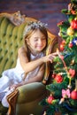Cute little girl sits on a sofa near a festive Christmas tree Royalty Free Stock Photo