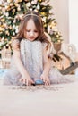 Cute little girl sitting against Christmas tree and playing with xmas decoration. Royalty Free Stock Photo