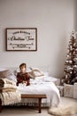 Cute little girl sitting on a big bed in a room with stylish Christmas decorations Royalty Free Stock Photo