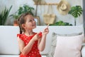 Cute little girl sitting on cozy sofa and pointing up on something intresting by fingers