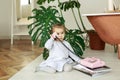 A cute little girl is sitting on the floor next to the bathtub and the monstera plant and talking on an old vintage pink push-butt Royalty Free Stock Photo