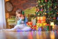 Cute little girl sitting on the floor in the room near the festive Christmas tree, holding a gift box