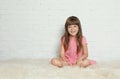 Cute little girl sitting on fur rug against brick wall Royalty Free Stock Photo