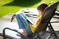 Cute little girl sitting in a garden and reading an ebook on sunny summer evening.