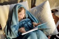 Cute little girl sitting in a garden under a blanket and reading a book on sunny summer evening