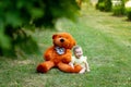 Cute little girl sitting on green grass with big Teddy bear in yellow summer dress in summer Royalty Free Stock Photo