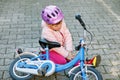 Cute little girl sitting on the ground after falling off her bike. Upset crying preschool child with safe helmet getting Royalty Free Stock Photo