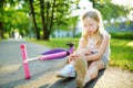 Cute little girl sitting on the ground after falling off her scooter at summer park. Child getting hurt while riding a kick