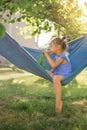 A cute little girl is sitting in a hammock and nibbling fresh sweet carrots Royalty Free Stock Photo