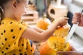 Cute little girl sitting on kitchen table, helping her father to carve large pumpkin, smiling. Halloween family background.