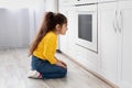 Cute little girl sitting near oven in kitchen and looking inside Royalty Free Stock Photo
