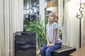 Cute little girl sitting near portable air purifier in the living room at home, new technology to protect