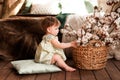 Cute little girl sitting on pillows near wicker basket with cotton flowers Royalty Free Stock Photo