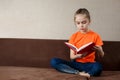 Cute Little Girl Sitting on The Sofa, reading a book, Distance learning Royalty Free Stock Photo