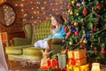 Cute little girl is sitting on the sofa in the room near the festive Christmas tree Royalty Free Stock Photo