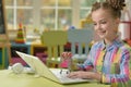 Portrait of cute little girl sitting at table with laptop and holding small shopping cart, online shopping concept Royalty Free Stock Photo