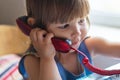 A cute little girl is sitting at a table and talking on an old red home landline phone. Communication, the concept of relationship Royalty Free Stock Photo